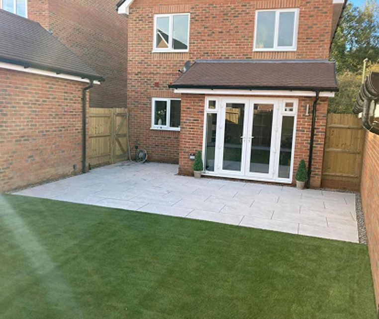 After: A modern patio with gray slabs leads to new PVC white French doors, bordered by artificial lawn.