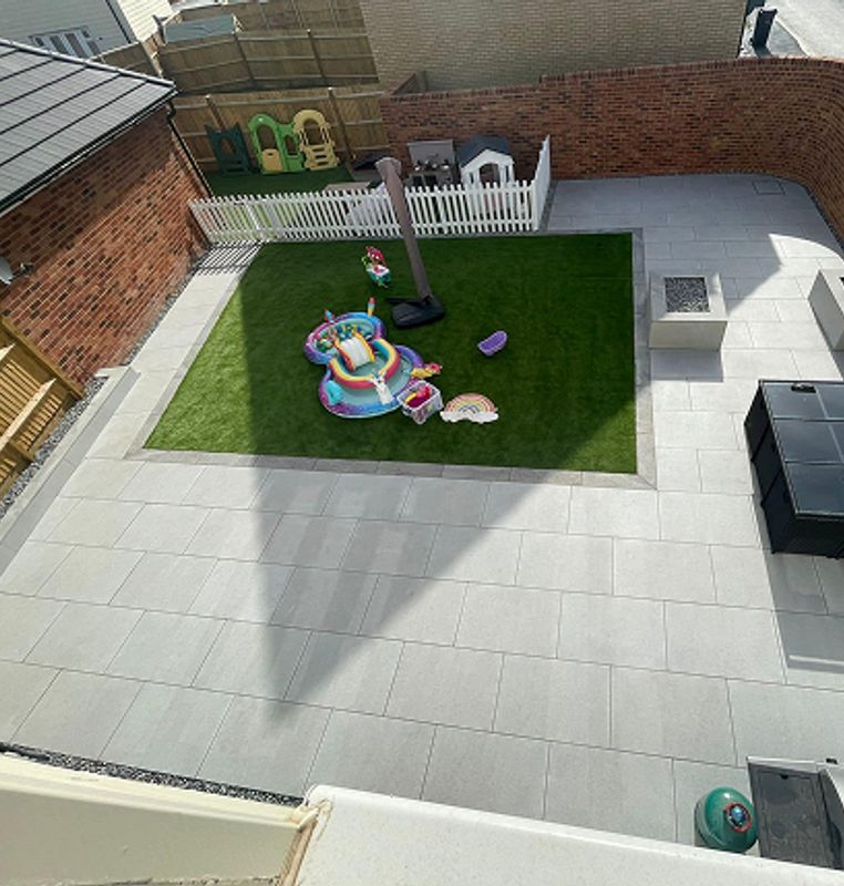 After: A transformed backyard featuring a sleek, modern patio with large light-grey tiles and a neatly bordered artificial grass play area, creating a stylish and functional space.