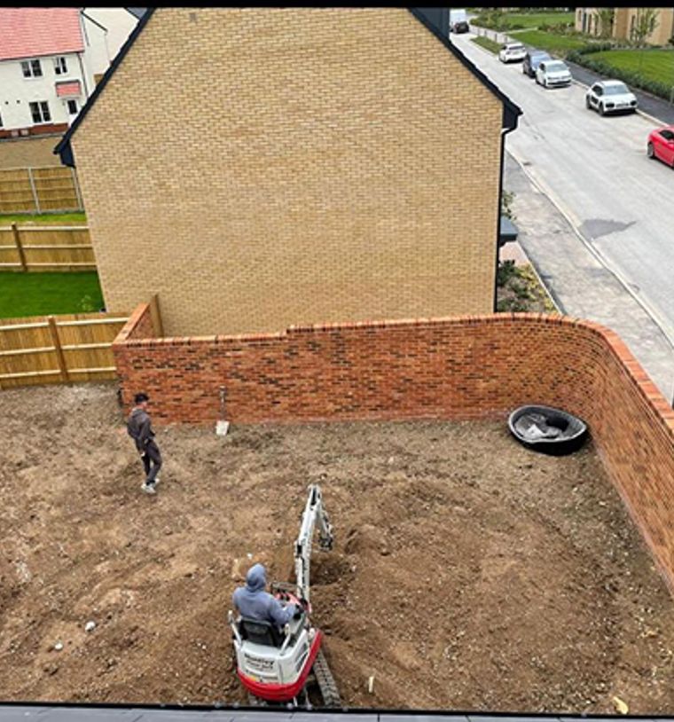 Before: A construction site in a residential area, where a worker operates a small excavator to prepare the ground. The site is enclosed by a curved brick wall.